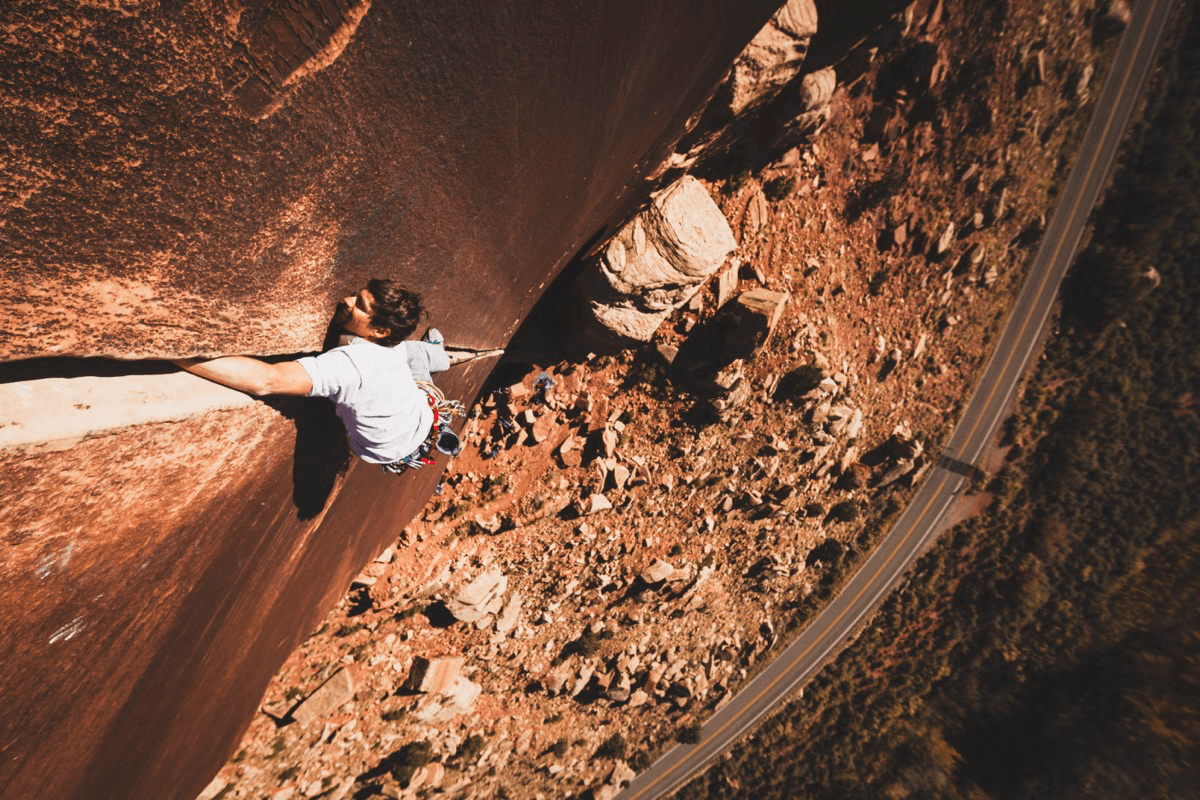 Climber on Super Crack of the Desert at Indian Creek, Utah — looking down the crack with the desert road visible far below